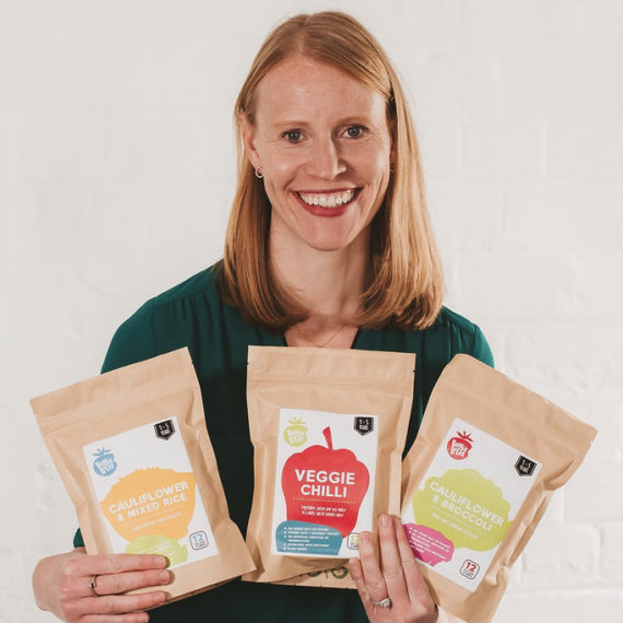 Hanna from Benji's Bites holding three pouches of her toddler food and smiling to the camera