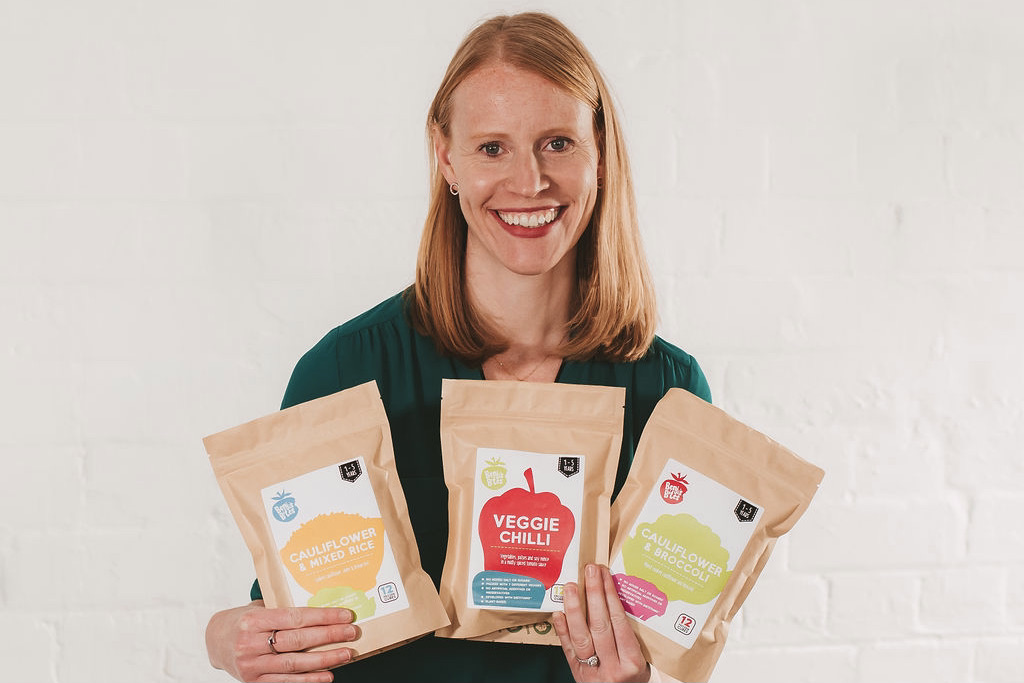 Hanna from Benji's Bites holding three pouches of her toddler food and smiling to the camera